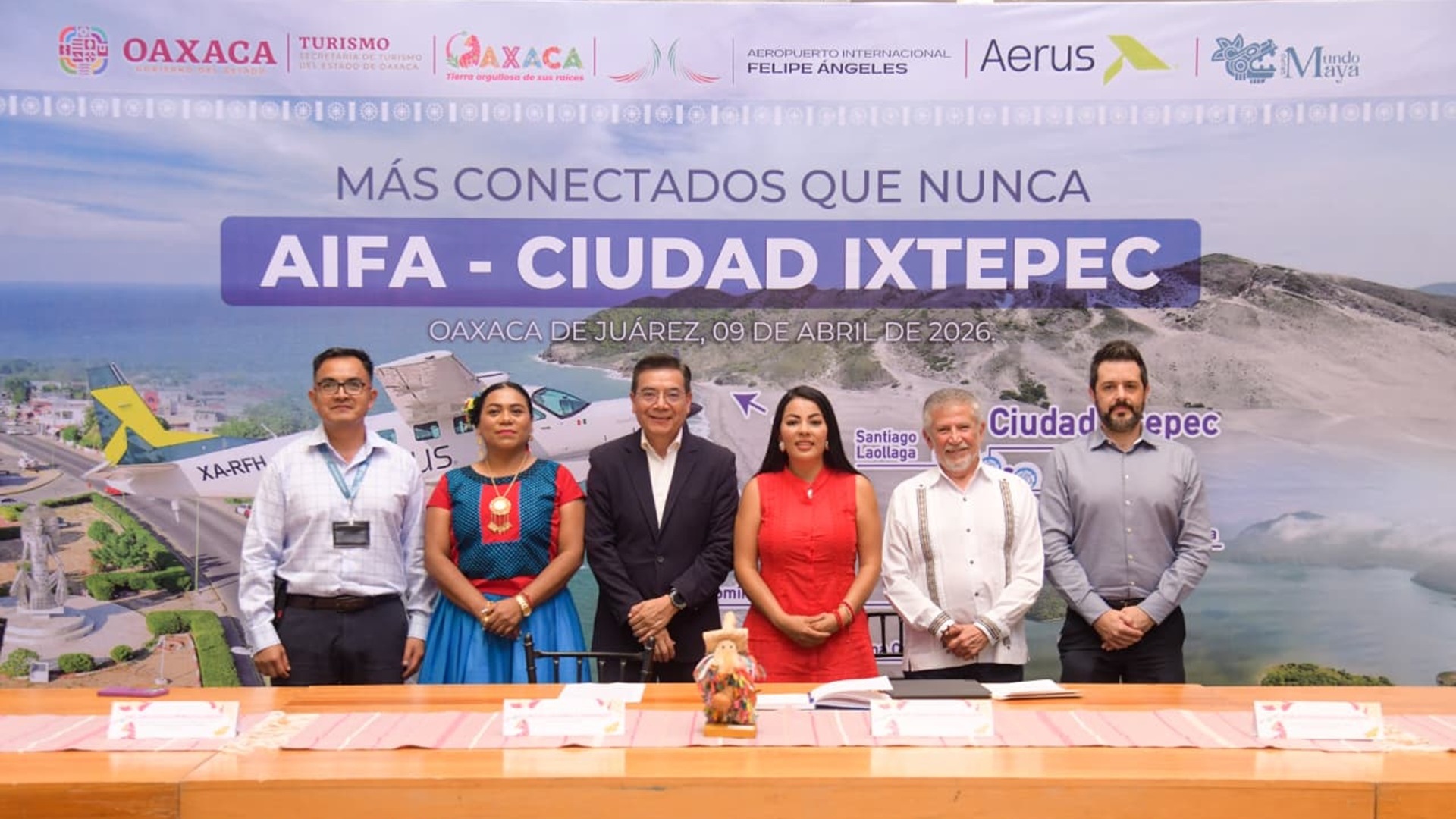 Saymi Pineda, titular de Sectur Oaxaca, con vestido rojo, junto a funcionarios anunciando una nuevo vuelo al Istmo.