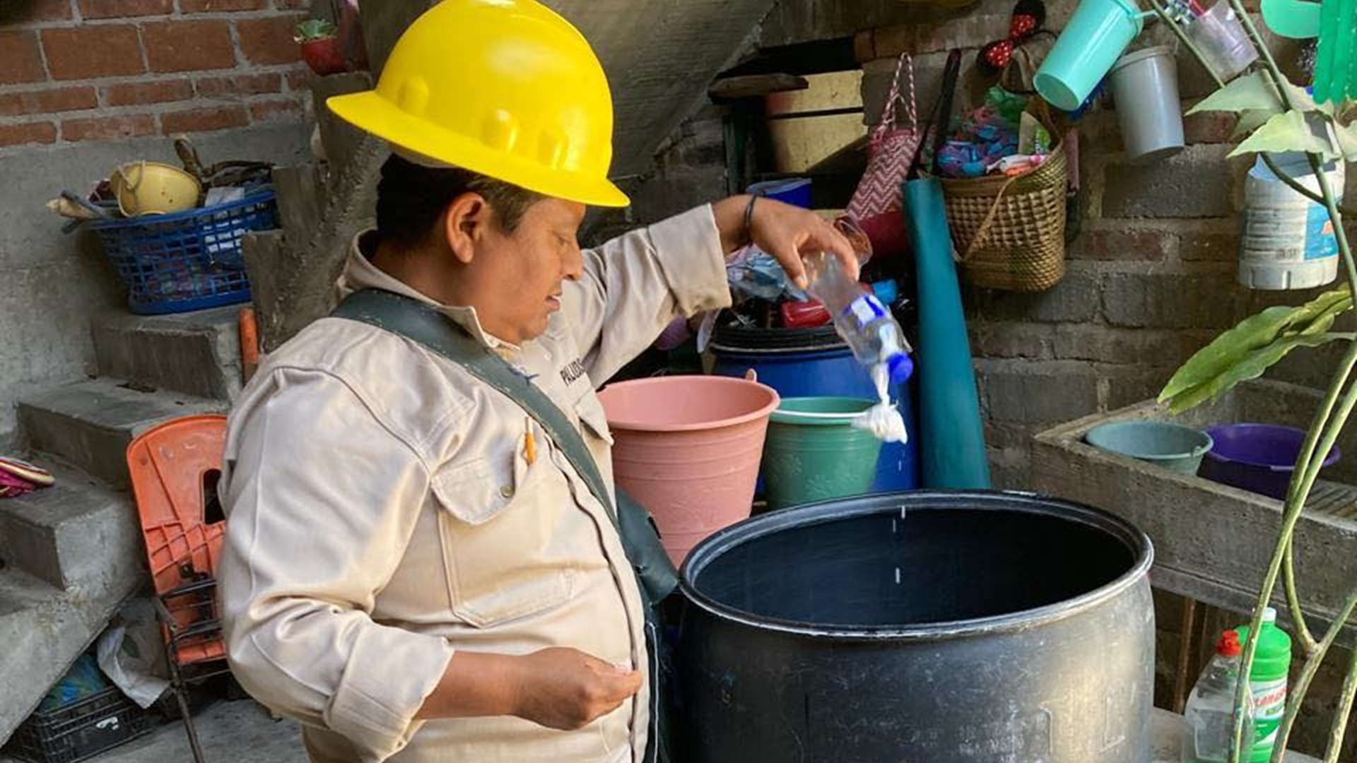 Hombre con overol y casco amarillo, de la brigada contra el dengue, deposita un líquido en otro recipiente.