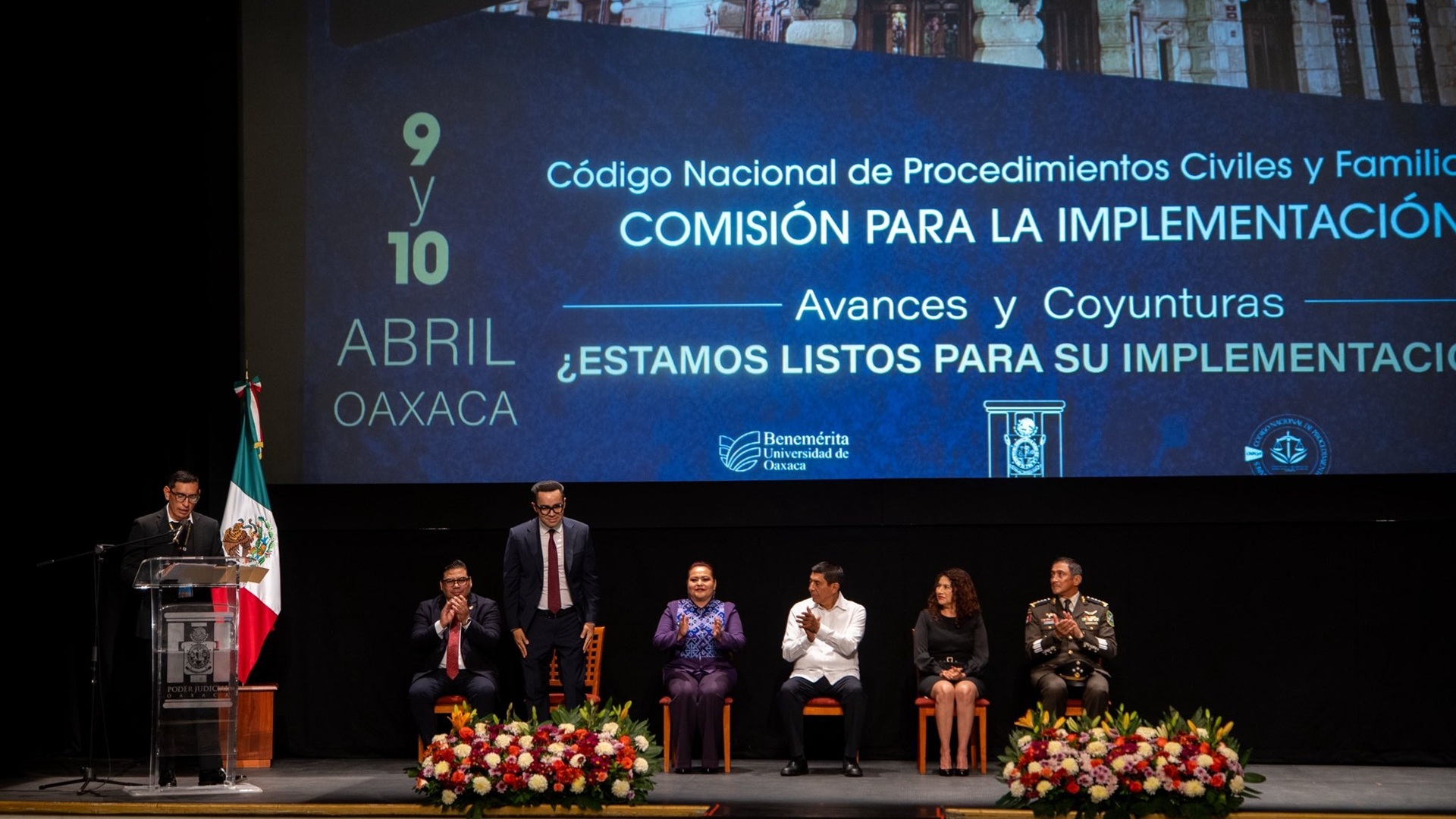 Magistrado Juan Carlos Díaz Carranza de cortaba roja y traje oscuro junto a autoridades de Oaxaca en el Teatro Macedonio Alcalá.