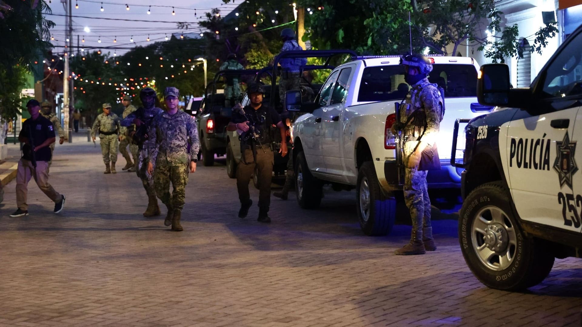 Varios elementos de la policía junto a camionetas con sirenas, estacionadas en una calle casi oscura.
