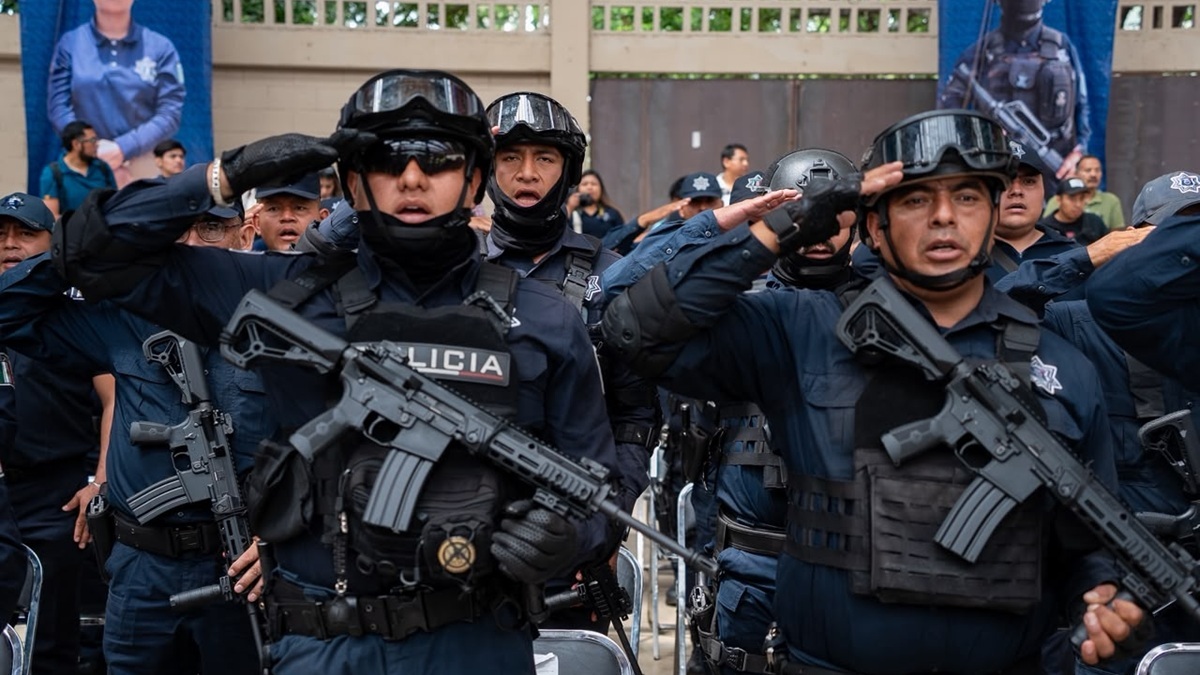 Agentes de seguridad de Oaxaca con uniformes negros y armas saludan a un auditorio que nos se ve en la imagen.
