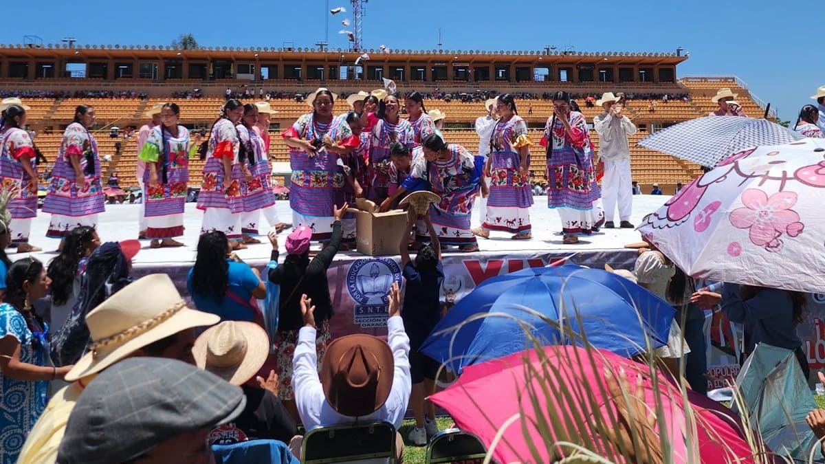 Danzantes mujeres sobre un templete en el Estadio Tecnológico de Oaxaca, interactuando con un público