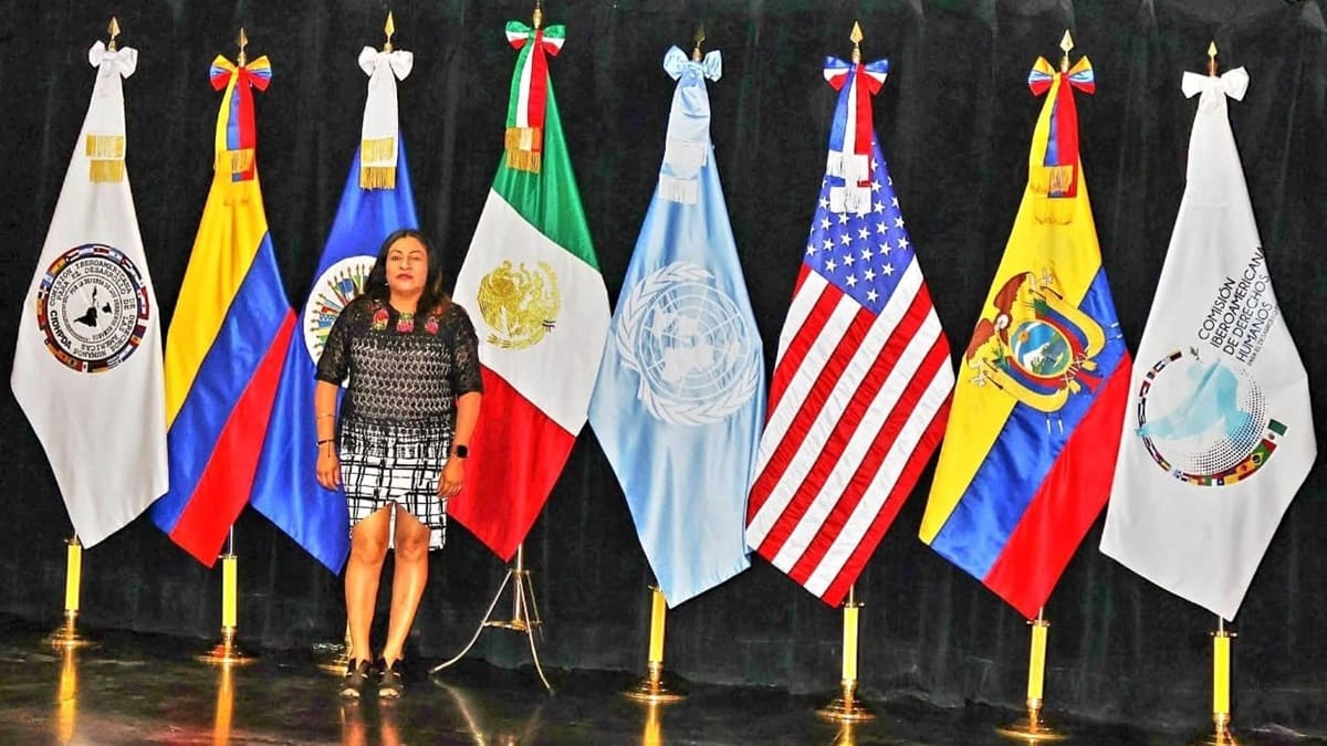 Rosa Delia Martínez posando en un escenario delante de múltiples banderas de distintos países del Mundo.