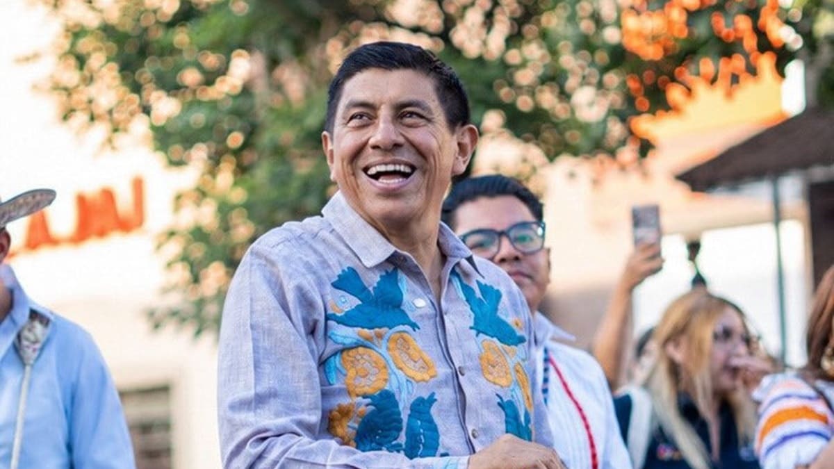 Salomón Jara sonríe acompañado por otras personas, mientras usa camisa con adornos regionales
