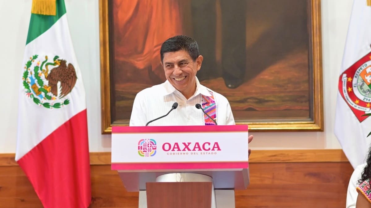 Salomón Jara Cruz sonriente en una conferencia de prensa junto a la bandera de México