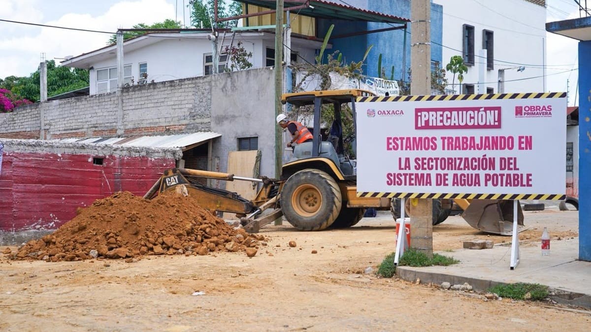 Trabajador con maquinaria pesada realiza una excavación junto a un letrero que advierte tener precaución 