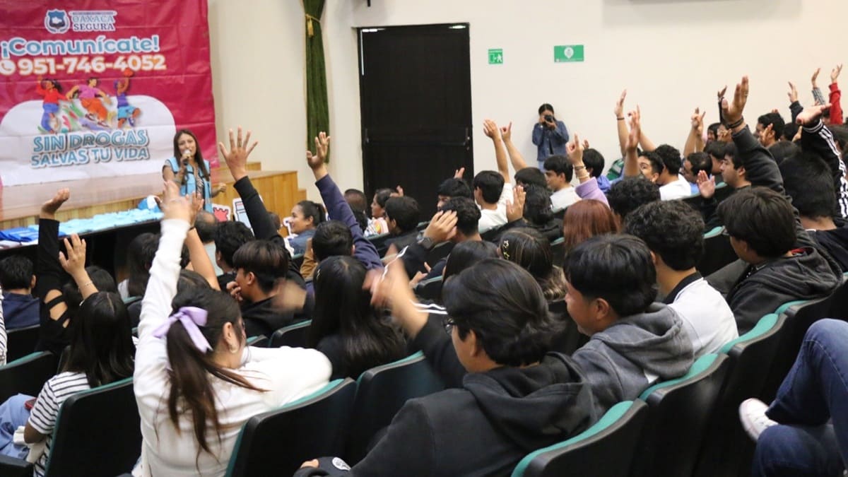 Mujer con chaleco morado habla en un auditorio ante jóvenes