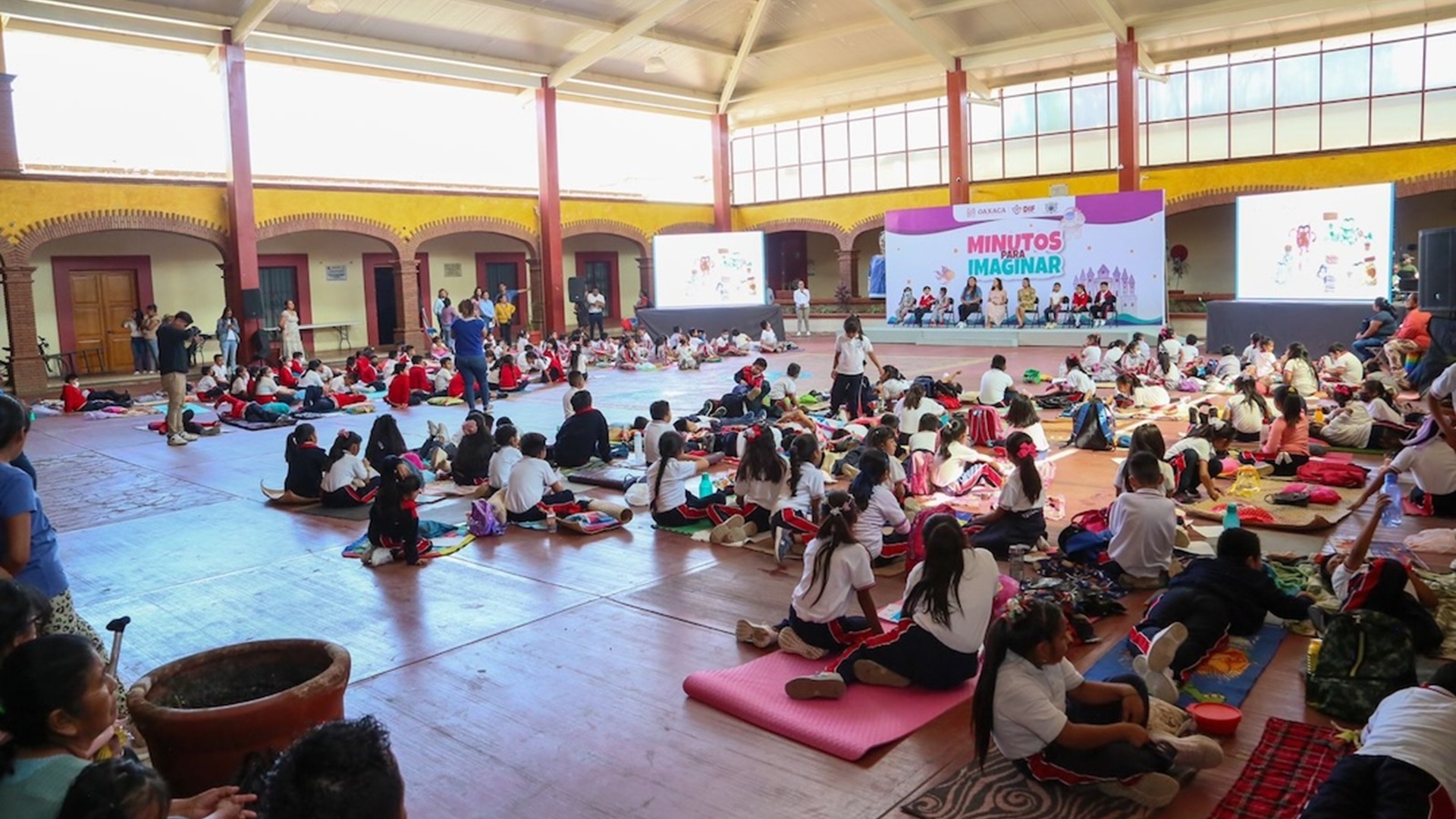 Decenas de ninos sentados en un salón de actividades.