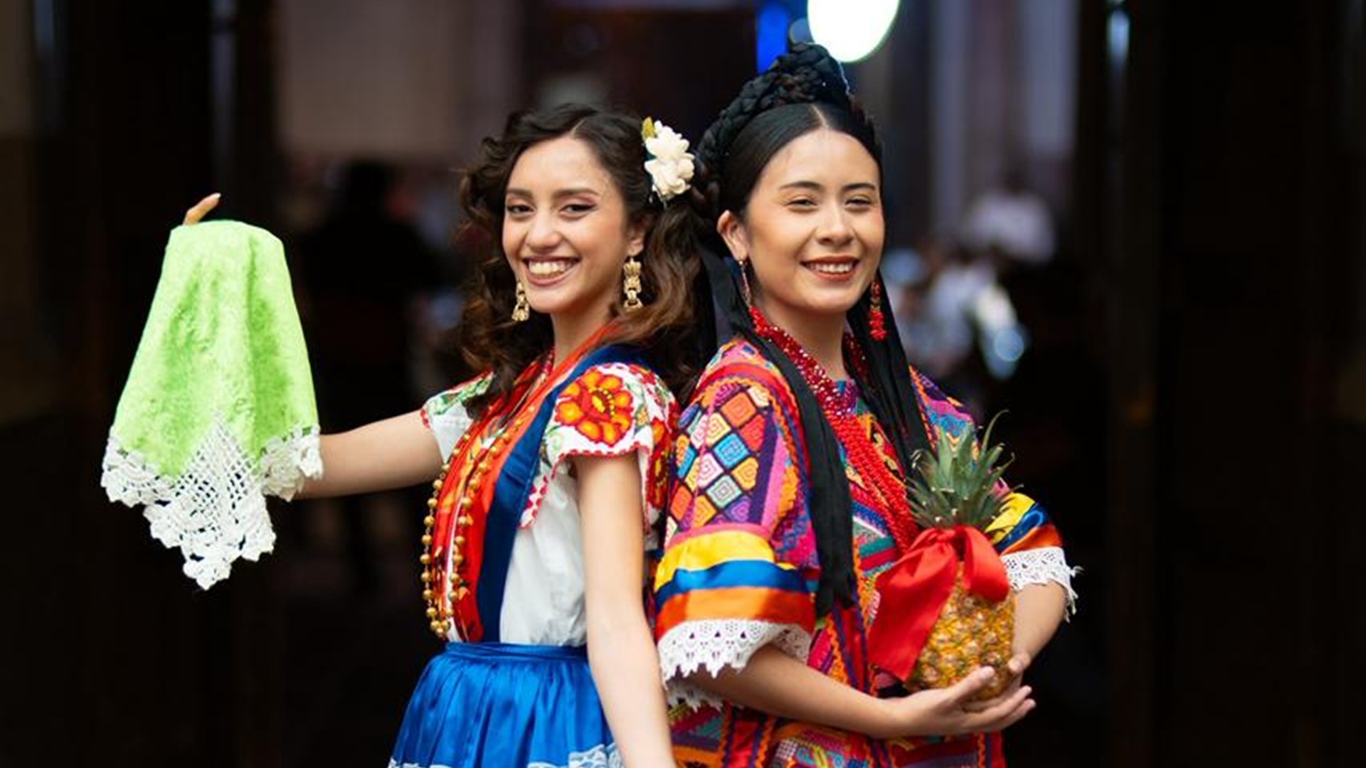 Dos mujeres, con trajes típicos de la Costa y la Cuenta de Oaxaca, sonríen a la cámara.