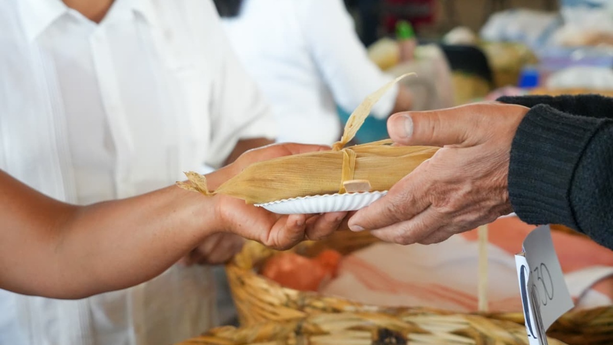 Las manos de una cocinera tradicional compartiendo un tamal a una persona