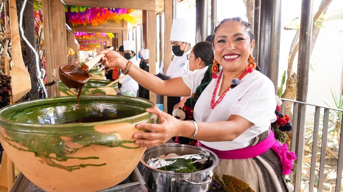 Mujer vestida con traje tradicional oaxaqueño sostiene una cuchara grande con mole tras sacarla de una cazuela