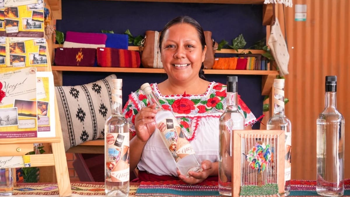 Artesana oaxaqueña con blusa típica regional exhibe botellas de mezcal en un mostrador
