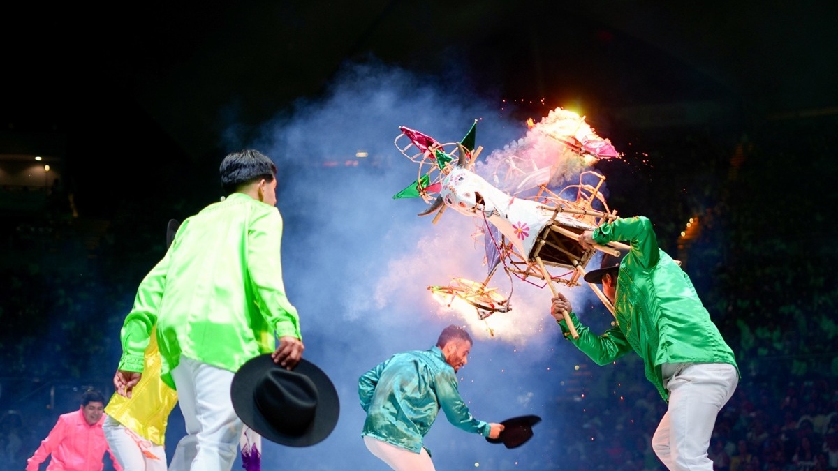 Dos danzantes sobre el escenario del Auditorio Guelaguetza realizan movimiento con un torito mientras se aprecia la pirotecnia.