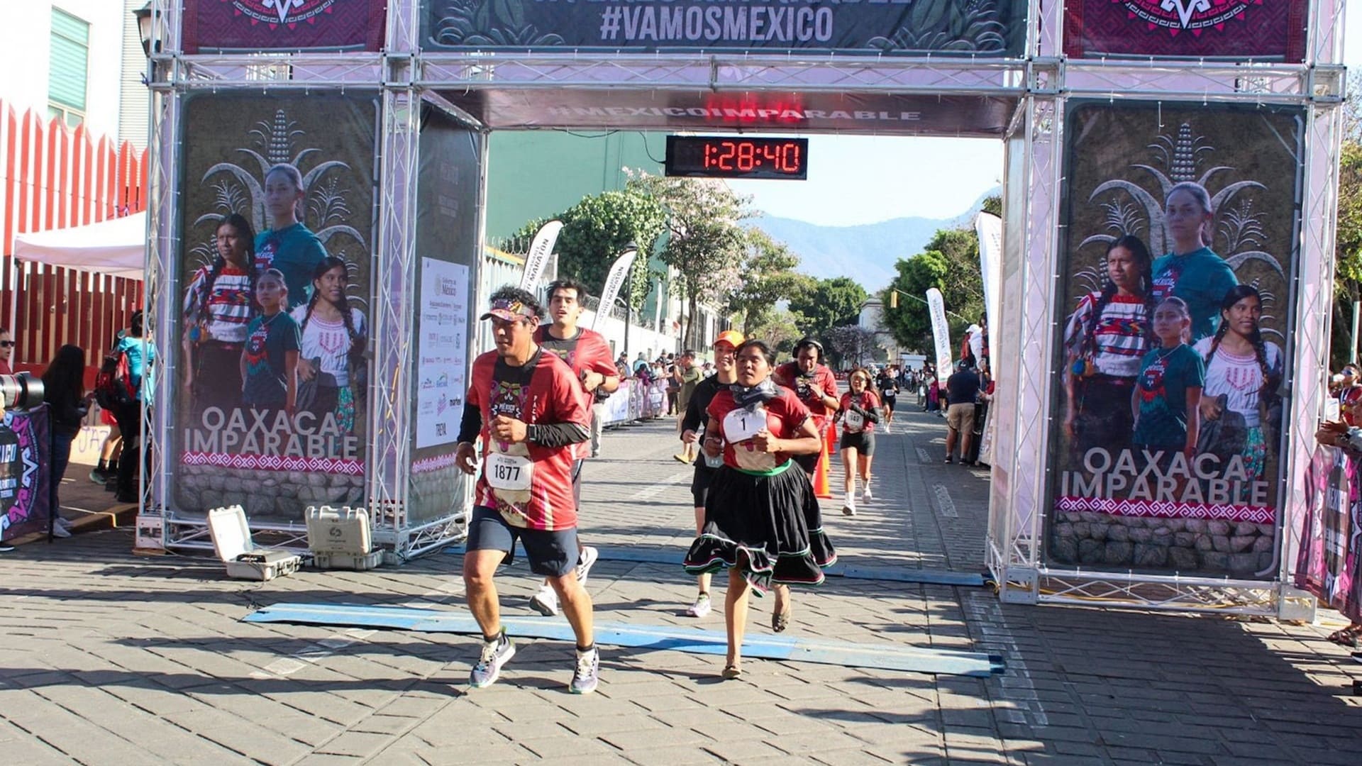 Un hombre y una mujer con vestido típico indígena atraviesan por una meta corriendo.