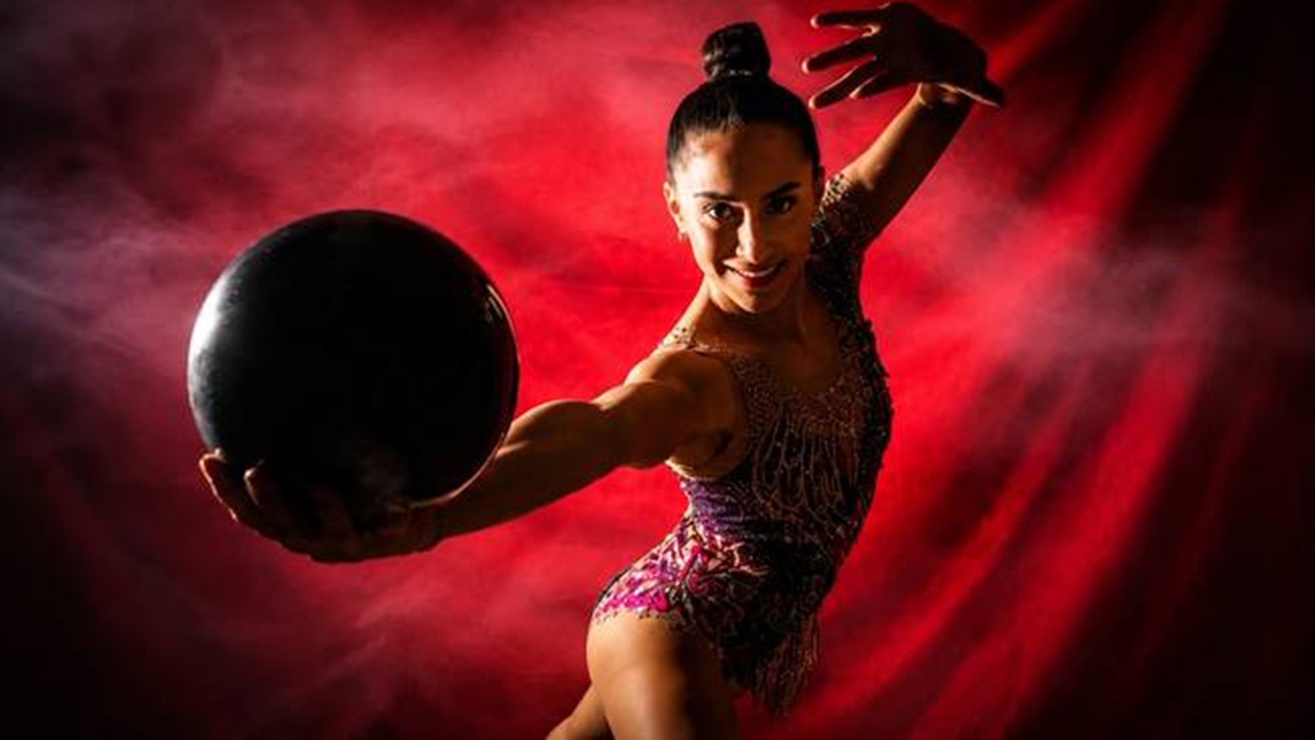 Mujer con traje rojo y en un fondo rojo sostiene una pelota.