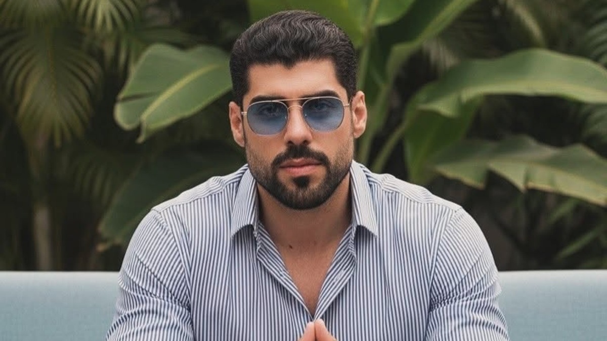 Masad Altamimi sentado, con barba, camisa de rayas y lentes oscuros en un jardín