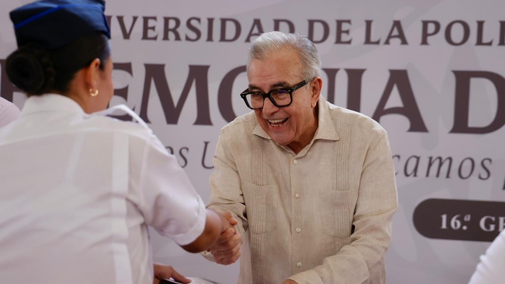 Rubén Rocha, con lentes, saluda a una mujer durante un acto público.