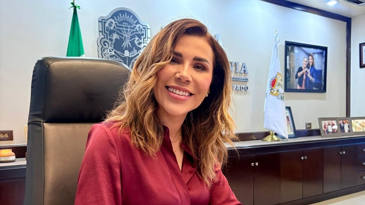 Marina del Pilar sentada en un escritorio sonriendo y sosteniendo un bolígrafo frente a una carpeta con documentos