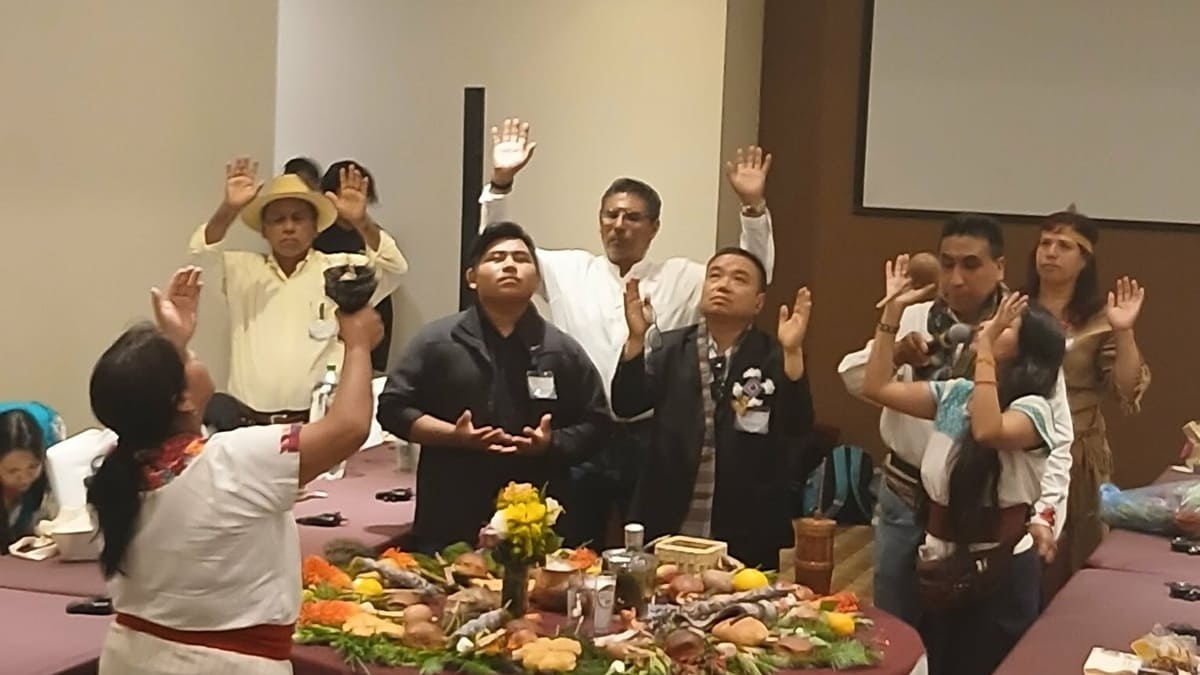 Representantes de pueblos indígenas entorno a una mesa con las manos levantadas y realizando un ritual 