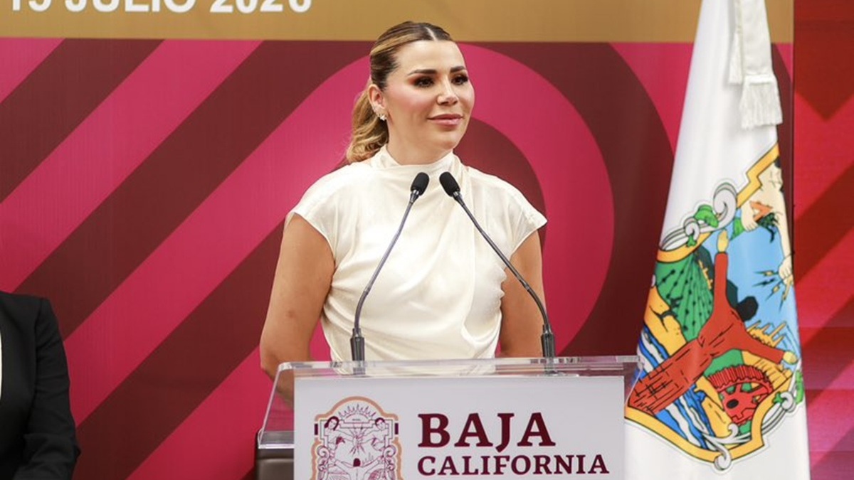 Marina del Pilar, Gobernadora de Baja California, con traje blanco y sonriente en una conferencia de prensa