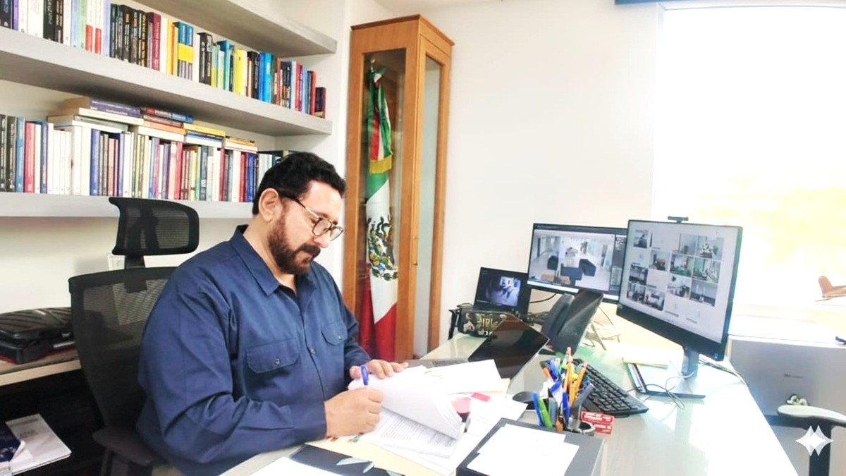 Ulises Lara en un escritorio tomando apuntes frente a dos monitores.