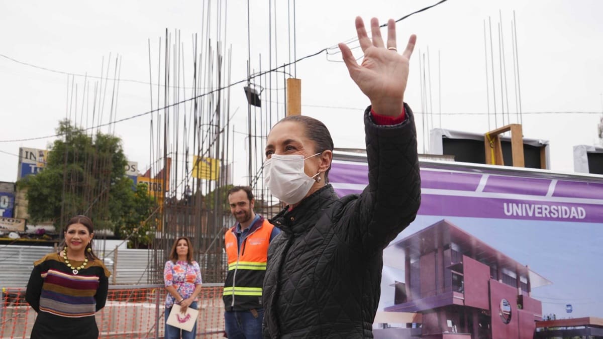 Claudia Sheinbaum con tapabocas levantando una mano mientras camina