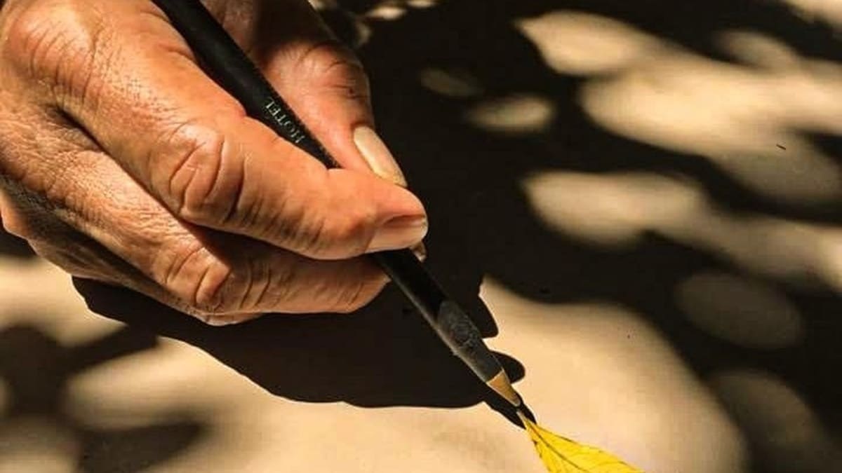 Imagen de una mano sosteniendo un lápiz junto a una hoja en un halo de luz