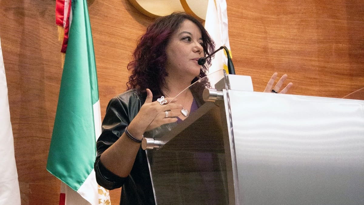 Wendy Figueroa Morales ofreciendo un mensaje desde un atril junto a la bandera de México.
