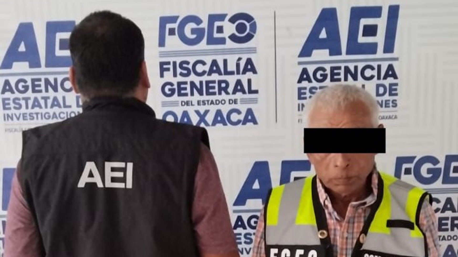 Un adulto mayor con chaleco amarillo y el rostro cubierto, acompañado de un agente de espaldas con chaleco negro.