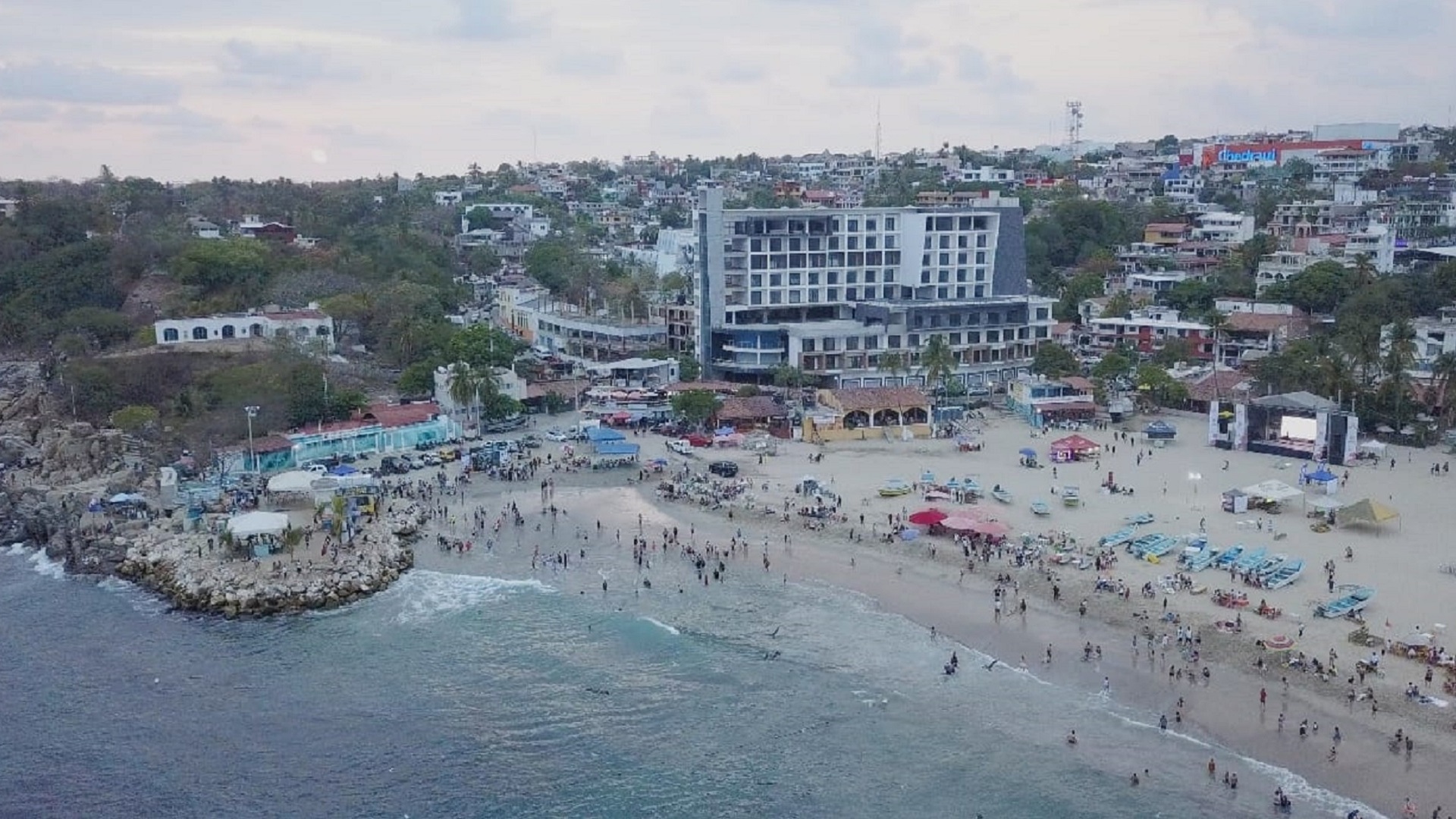 Imagen aérea de una playa, mar azul y una pila de rocas en desorden.