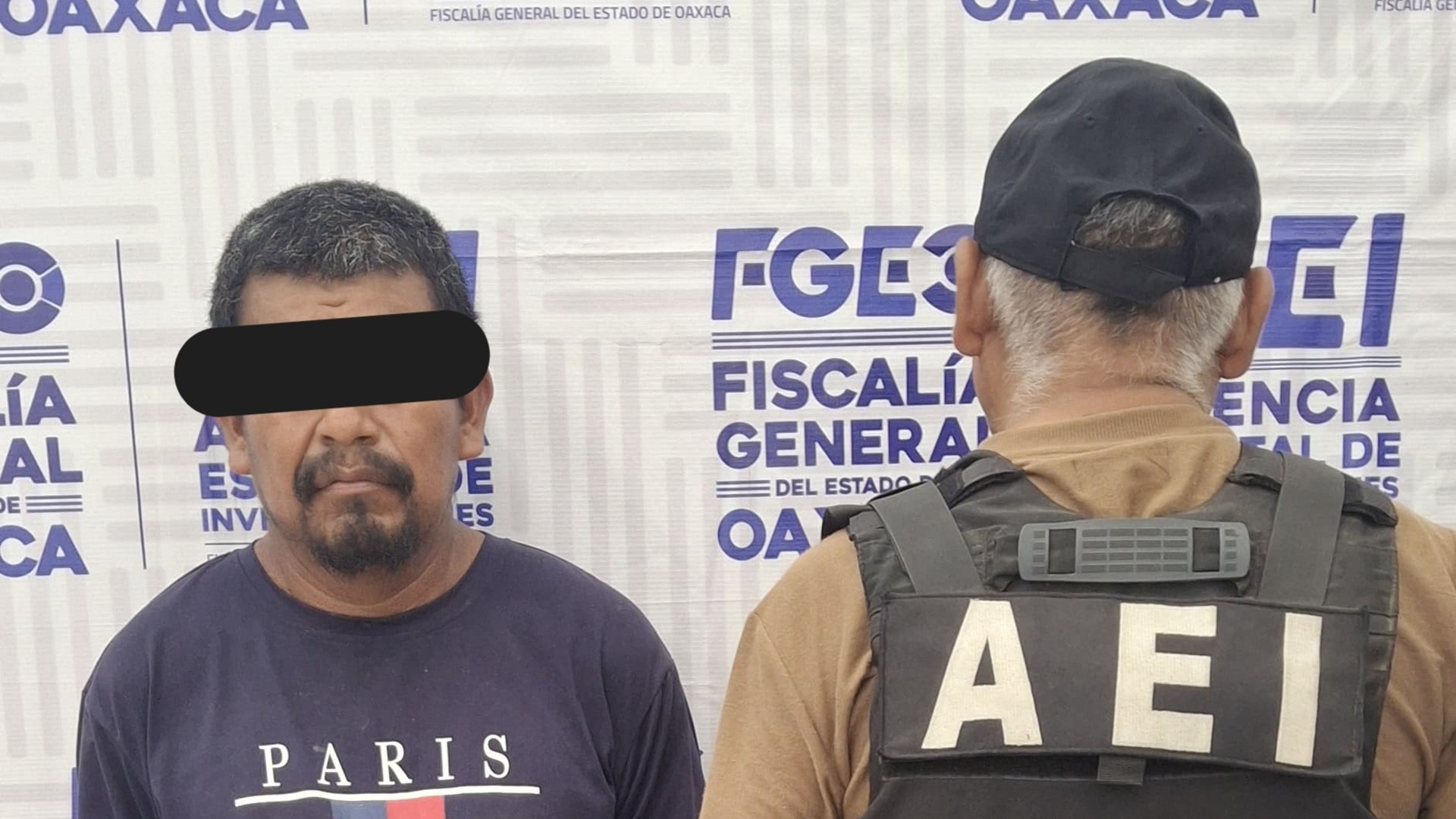 Un hombre con el rostro cubierto es presentado como detenido por un agente de espaldas y con gorra negra.