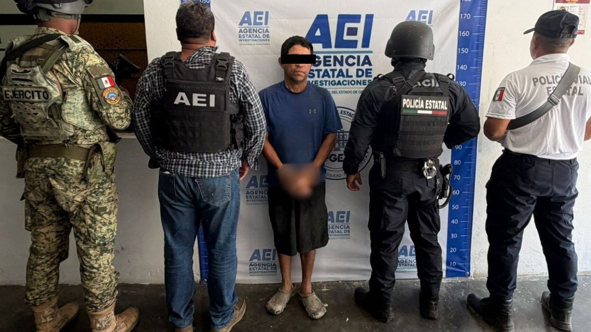 Hombre joven vestido de negro y rostro protegido custodiado por policías.