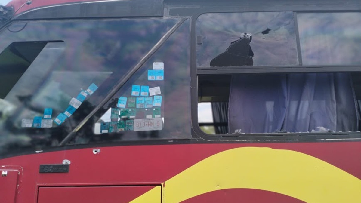 Vista lateral de autobús pintado de rojo con los cristales rotos por disparos de arma de fuego