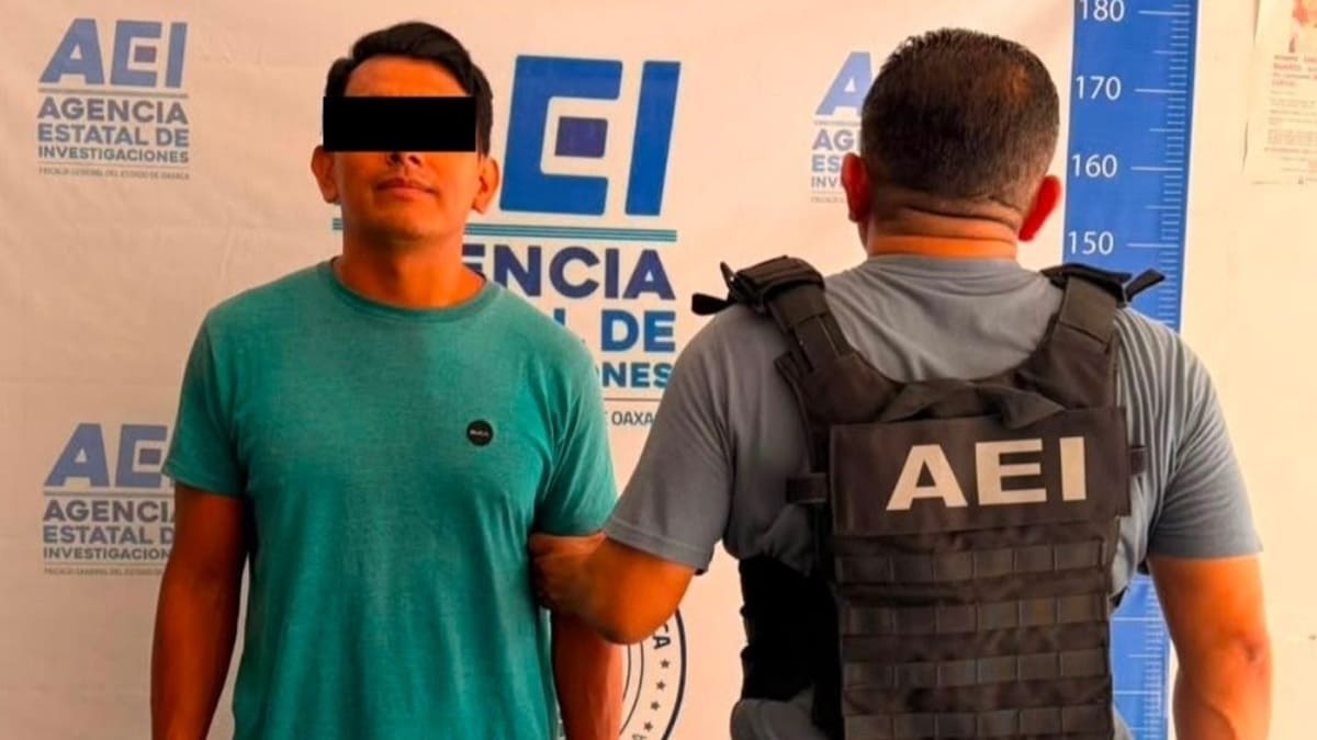 Hombre joven con playera verde y los ojos protegidos por mandato de ley es custodiado por un agente de seguridad