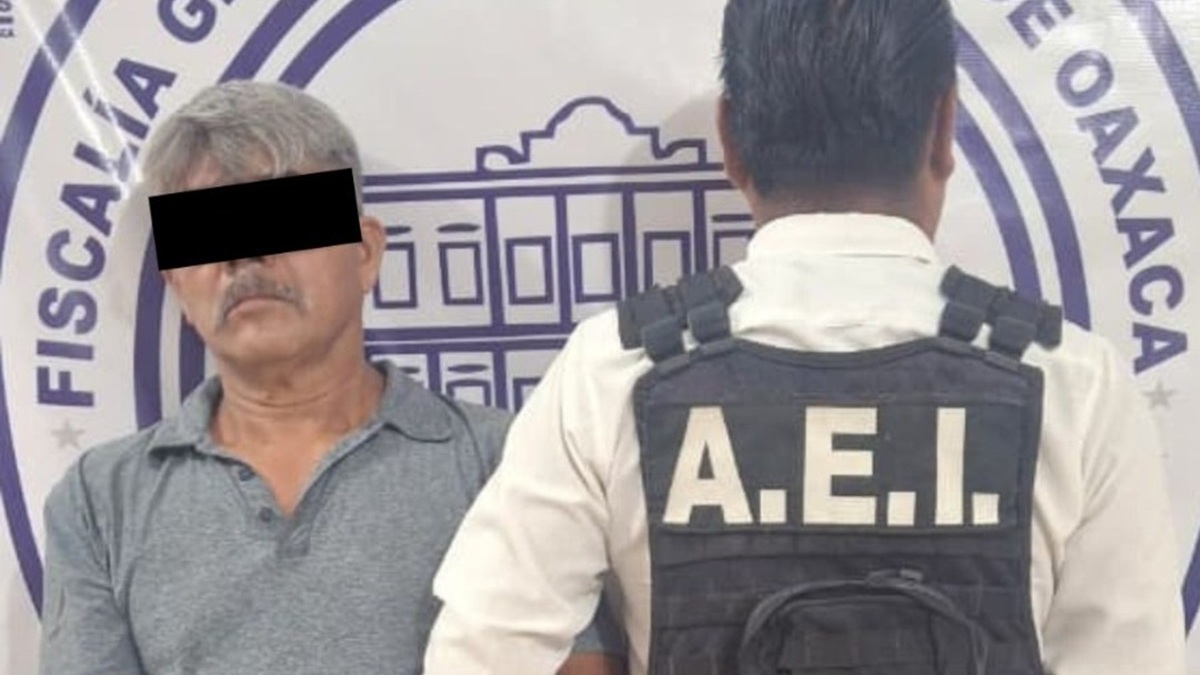 Adulto mayor en short, con las manos esposadas y los ojos cubiertos por ley, custodiado por un agente