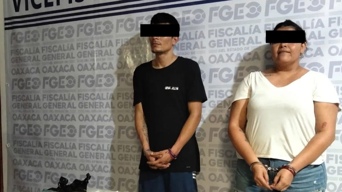 Un hombre y una mujer jóvenes esposados y con los ojos protegidos por una banda negra por mandato de ley