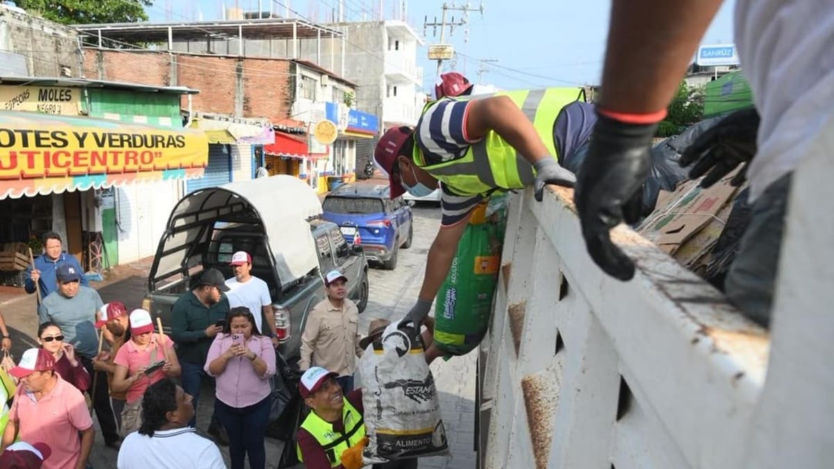Salomón Jara entrega una bolsa a una persona sobre un camión, junto a otras personas en una calle de Puerto Escondido