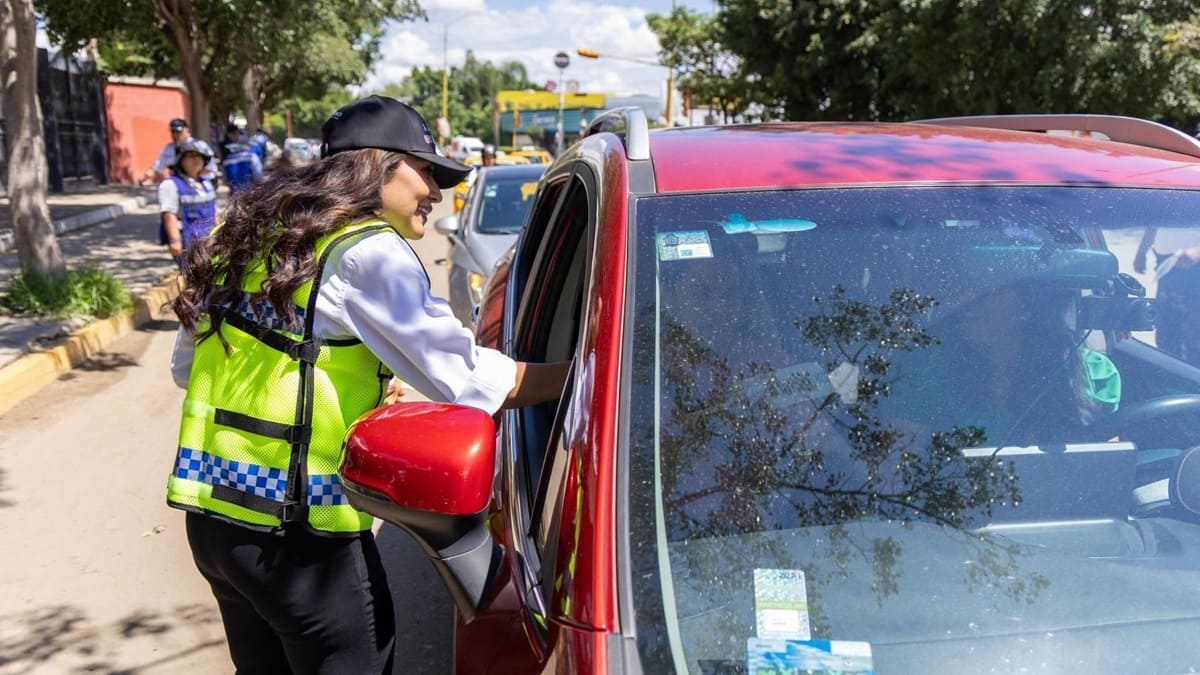 Mujer con chaleco verde conversar con el conductor de un vehículo rojo